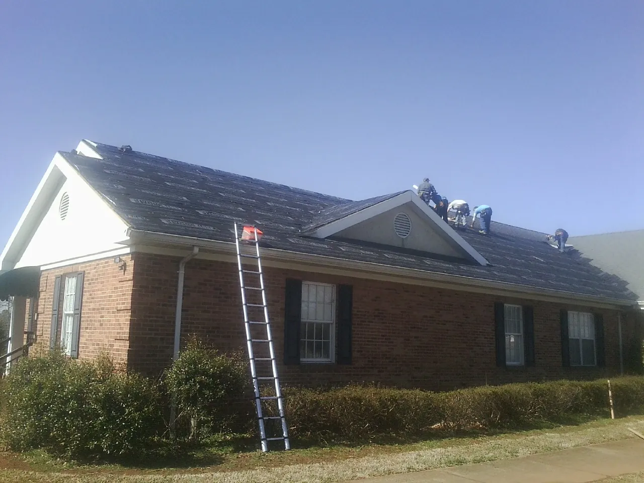 Crew tearing shingles off a brick ranch roof with a ladder set — Emergency Roof Repair work by our crew in Ellsworth